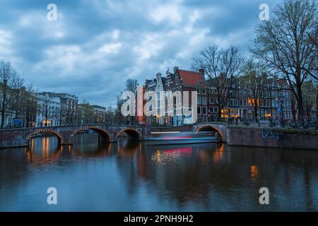 Les ponts s'illuminent à l'heure bleue du crépuscule à Amsterdam, Hollande, pays-Bas en avril - exposition longue avec des lumières de bateau passant sous le pont Banque D'Images