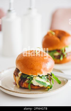 Deux délicieux hamburgers faits maison avec du bœuf, du fromage et des légumes sur une table en bois blanc Banque D'Images