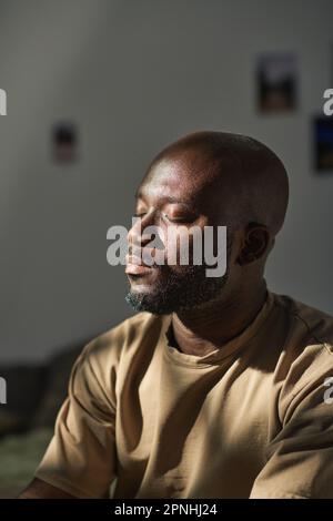 Image verticale de l'homme afro-américain assis avec ses yeux fermés et méditant à la maison Banque D'Images