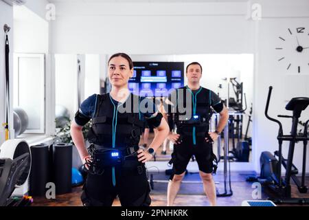 Quelques personnes dans les combinaisons ems se préparent pour l'entraînement dans le club de fitness ou la salle de gym. Les jeunes hommes et les jeunes femmes sont debout, les mains sur leur ceinture. Équim. Sport Banque D'Images