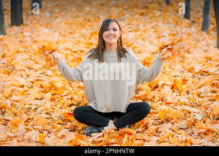 Jeune femme souriante s'amusant dans le parc d'automne se préparer jette des feuilles sucrée Banque D'Images
