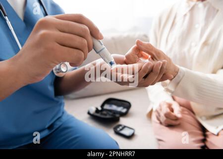 vue rognée d'une infirmière multiraciale prenant un échantillon de sang d'une femme âgée avec un stylo lancet Banque D'Images