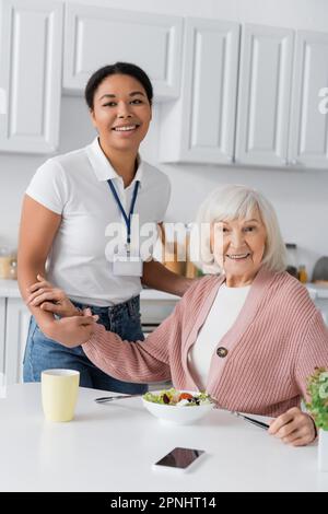 joyeux travailleur social multiracial tenant les mains d'une femme reconnaissante à la retraite tout en regardant la caméra Banque D'Images