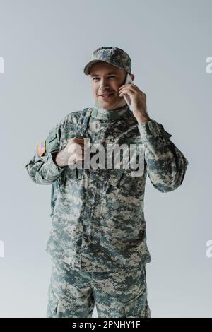 joyeux militaire en uniforme parlant sur smartphone isolé sur gris Banque D'Images