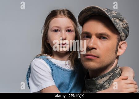 enfant patriotique embrassant son père en uniforme militaire et pleurant pendant la journée du souvenir, isolé sur des gris Banque D'Images