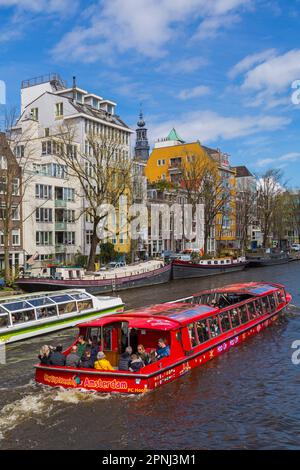 Les touristes qui visitent la ville d'Amsterdam sautent sur le bateau à arrêts multiples qui longe le canal et passe devant des bateaux à Amsterdam, Hollande, pays-Bas en avril Banque D'Images