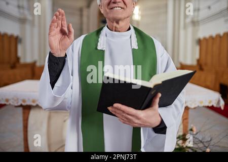 Gros plan du prêtre senior en tenue de cérémonie debout avec les croyants de la Bible et de la bénédiction pendant la cérémonie dans l'église Banque D'Images