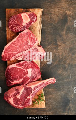 Steaks de première qualité crus. Variété de steaks de viande de choix angus noir frais T-bone, New York, Ribeye, striploin, Tomahawk planche à découper sur fond noir ou foncé Banque D'Images