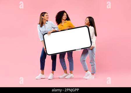 Jeunes femmes diverses tenant un smartphone géant avec une maquette pour la publicité, démontrant l'espace pour votre conception, sur toute la longueur Banque D'Images