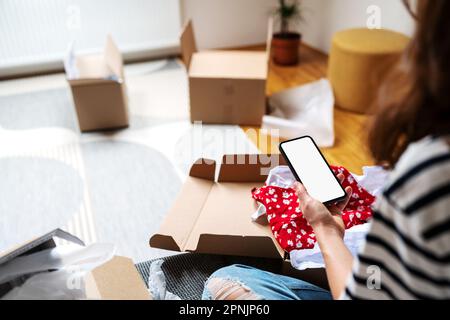 Image de maquette de smartphone avec écran vide dans la main de la femme sur le fond des boîtes en carton ouvertes. Banque D'Images