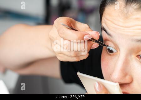 photo détaillée d'une adolescente de latina, en appliquant soigneusement ses faux cils avec des pinces Banque D'Images