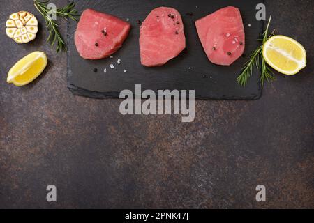Fruits de mer. Steaks de thon juteux cru aux épices et au romarin sur une table en pierre. Vue de dessus. Copier l'espace. Banque D'Images