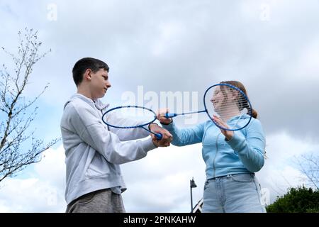 Badminton raquettes garçons fille balançoire les uns les autres avec raquette arrière-plan de jeu de ciel ayant plaisir Premier amour relation adolescent en colère être satisfait sourire émotions transition âge jeunes hommes et femmes Banque D'Images