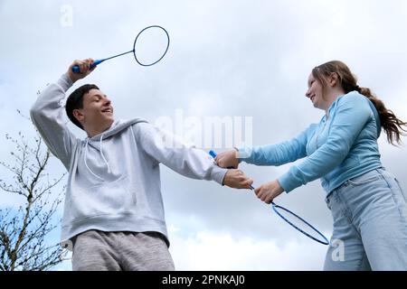 Badminton raquettes garçons fille balançoire les uns les autres avec raquette arrière-plan de jeu de ciel ayant plaisir Premier amour relation adolescent en colère être satisfait sourire émotions transition âge jeunes hommes et femmes Banque D'Images