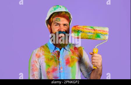 Peintre homme. Peintre souriant dans un casque de sécurité avec rouleau de peinture. Employé barbu avec rouleau de peinture. Peintre professionnel, décorateur, ouvrier de construction Banque D'Images