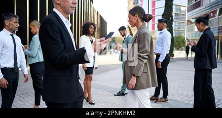 Hommes et femmes d'affaires utilisant le téléphone mobile tout en allant au bureau dans une rue bondée. Banque D'Images