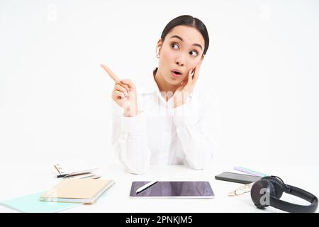 Portrait d'une femme d'affaires asiatique assis au bureau avec une tablette, des points à gauche et des sourires, des spectacles publicitaires, une bannière de bureau, un fond blanc Banque D'Images