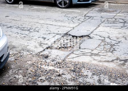 Vue sur une grande rue résidentielle de Pothole, tarmac brisé avec un grand trou dans la surface Banque D'Images