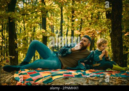 En-cas sain. Pique-nique en famille. Un père à barbe d'un petit garçon passe du temps dans la forêt. Un homme barbu brutal et un petit garçon mangent des pommes. Pique-nique en forêt Banque D'Images