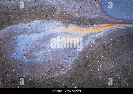 Taches d'huile dues à des fuites dans le moteur de la voiture. L'huile après la pluie fait des taches avec des reflets arc-en-ciel spectre de réfraction du soleil. Banque D'Images