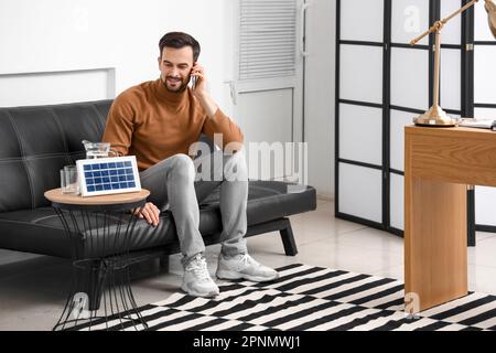 Beau homme parlant par téléphone portable près du panneau solaire portable à la maison Banque D'Images