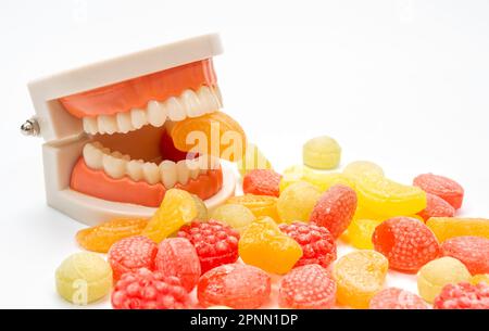 Une variété de bonbons de couleur sur fond blanc, avec un modèle de dent piquant l'une des bonbons Banque D'Images