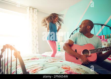 Vous rock, papa. une petite fille gaie sautant sur son lit à la maison pendant que son père joue de la guitare. Banque D'Images