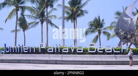 Un homme marche à côté d'un panneau 'Jomtien Pattaya Beach' à la station balnéaire de Jomtien, Pattaya, Thaïlande, Asie. Palmiers en arrière-plan. Banque D'Images