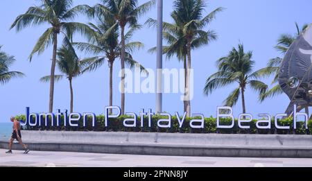 Un homme marche à côté d'un panneau 'Jomtien Pattaya Beach' à la station balnéaire de Jomtien, Pattaya, Thaïlande, Asie. Palmiers en arrière-plan. Banque D'Images