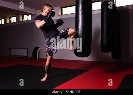 Un jeune homme participe à une séance d'entraînement, pratiquant ses compétences de boxe en exécutant un puissant coup de pied Banque D'Images