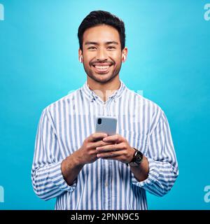 Heureux, portrait et un homme avec un téléphone pour la communication isolé sur un fond bleu dans un studio. Sourire, mise à jour sur les réseaux sociaux et une personne qui tape dessus Banque D'Images