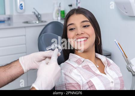 Croissez le stomatologiste mâle anonyme en gants expliquant comment utiliser les aligneurs de dents à la positive hispanique adolescente lors de la consultation dans les cliniques dentaires Banque D'Images