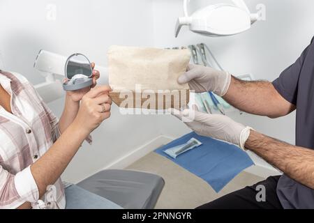 Un dentiste masculin méconnaissable donne un sac à main avec des fournitures dentaires pour couper l'adolescent avec une boîte de retenues pendant qu'il travaille en clinique Banque D'Images