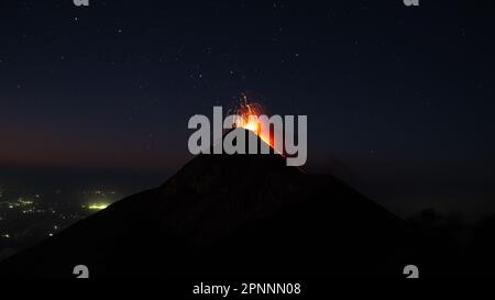 Un cliché spectaculaire d'une éruption volcanique, avec un nuage de cendres et de lave qui s'élève du sommet la nuit Banque D'Images