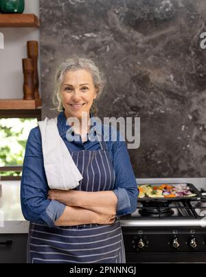 Portrait d'une femme caucasienne âgée heureuse portant un tablier et souriant dans la cuisine Banque D'Images