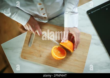 Gros plan sur la main d'une femme caucasienne inconnue tenant un couteau coupant des oranges copier l'espace Banque D'Images