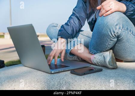 Gros plan des femmes travaillant à distance à l'aide d'un ordinateur portable et d'un smartphone assis à l'extérieur. Freelance, nomade numérique, concept d'e-commerce Banque D'Images