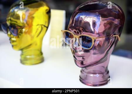 Deux têtes de femme en verre coloré, teintées en violet et jaune, portant des lunettes dans une vitrine d'opticien Banque D'Images