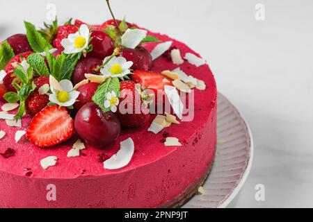 Dessert végétalien. Gâteau aux fruits frais à la noix de cajou avec fraises fraîches et cerises dans une assiette. Gros plan. Alimentation saine Banque D'Images