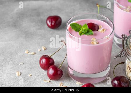 Yaourt aux baies de cerisier ou yaourt dans des verres avec baies fraîches, flocons d'avoine, menthe pour un petit déjeuner sain sur fond gris. Nourriture savoureuse Banque D'Images