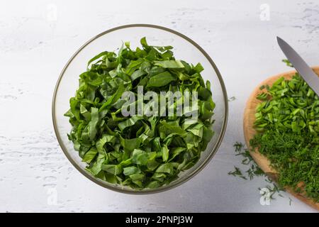 Bol en verre avec épinards hachés et une planche avec oignon et aneth sur fond bleu clair, vue du dessus. Cuisiner des aliments végétaliens sains Banque D'Images