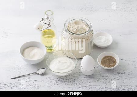 Ingrédients pour la cuisson maison: Oeuf, crème aigre (yaourt), sucre, sucre vanillé, farine, huile végétale, poudre à lever, sel sur fond bleu clair Banque D'Images