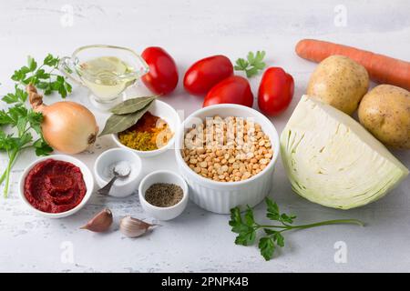 Ingrédients pour ragoût de légumes : pois, pommes de terre, chou, carottes, oignons, ail, tomates, huile végétale, pâte de tomate, herbes, sel et épices sur un l Banque D'Images
