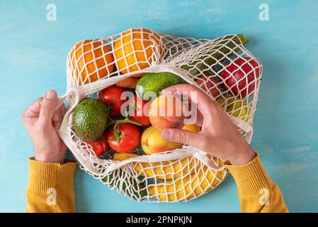 Homme poignet prenant des fruits de pêche du sac de shopping de filet avec des fruits et des légumes. Magasins écologiques. Style de vie durable, zéro déchet, sans plastique Banque D'Images