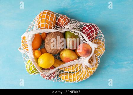 Vue de dessus du sac à provisions en maille avec des fruits tropicaux écologiques bio sur fond bleu. Respect de l'environnement et concept sans plastique Banque D'Images