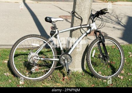 Le vélo repose sur l'herbe verte, s'appuie contre un poteau et se verrouille Banque D'Images