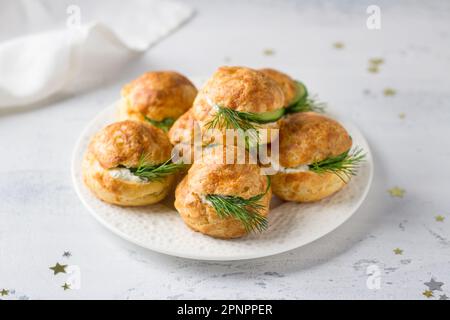 Des profiteroles au fromage à la crème, au concombre et aux herbes, aux gougres, aux pâtisseries françaises traditionnelles, dans une assiette blanche sur fond gris clair, en haut vie Banque D'Images