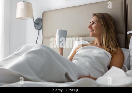 jeune femme souriante au lit et prenant le café du matin dans la chambre à la maison Banque D'Images