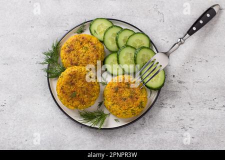 De délicieuses côtelettes de millet avec carottes et graines servies avec concombre et herbes sur fond texturé gris, vue du dessus. Cuisine végétalienne maison Banque D'Images