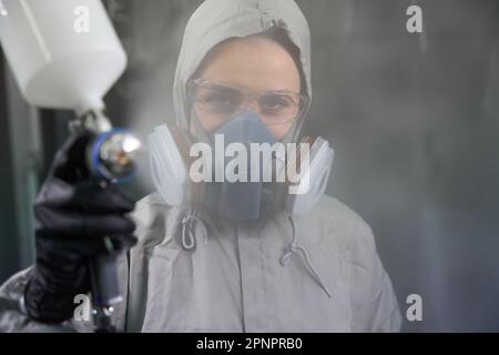 Femme spécialiste automobile travaillant avec un pistolet à peinture dans une cabine de peinture Banque D'Images
